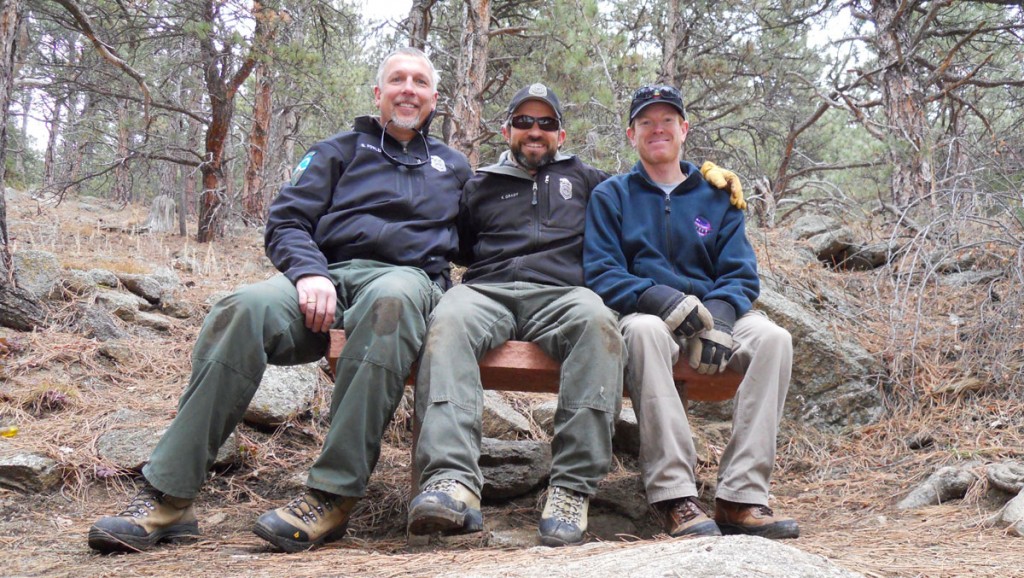 Three smiling park rangers sit on a bench