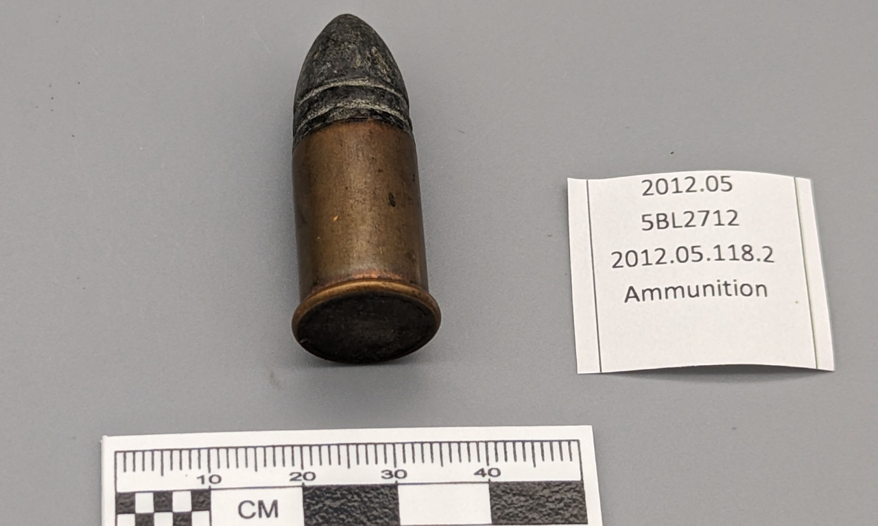 An ammunition shell with a ruler and card showing it's artifact collection number.