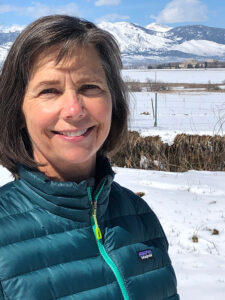 Woman smiles into the camera with a snowy scene behind her.