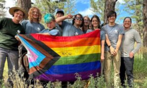 A group of smiling youth hold up a Pride flag.