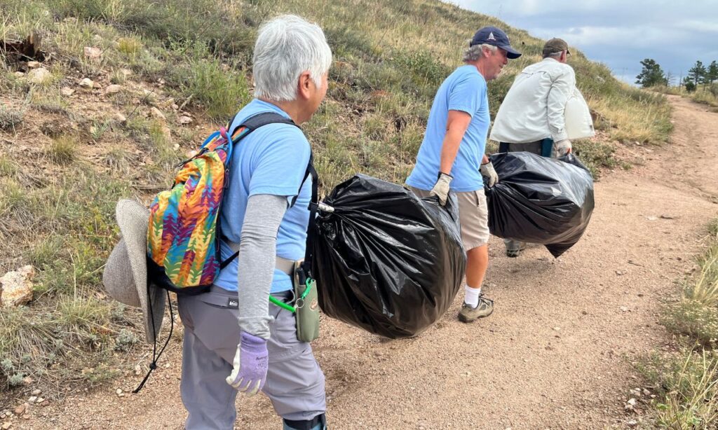 Three volunteers carry large black trash bags on a mountainous trail. 