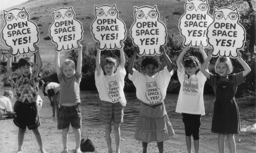 Six children hold up signs that read, "Open Space Yes!" The signs are shaped like owls.