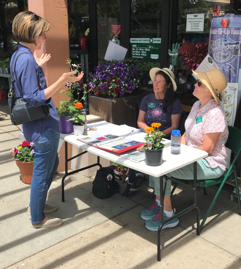 Volunteers sit at a table in front of the garden center answering questions from a shopper