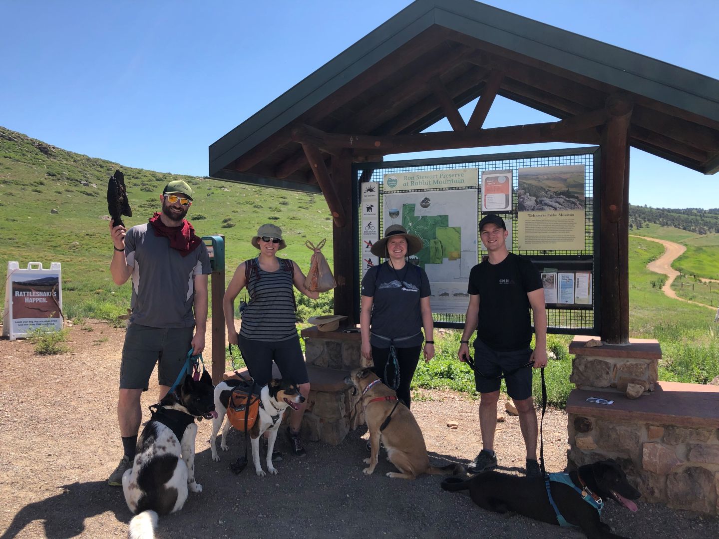 A group of dog walkers holding up bags of trash on a trail