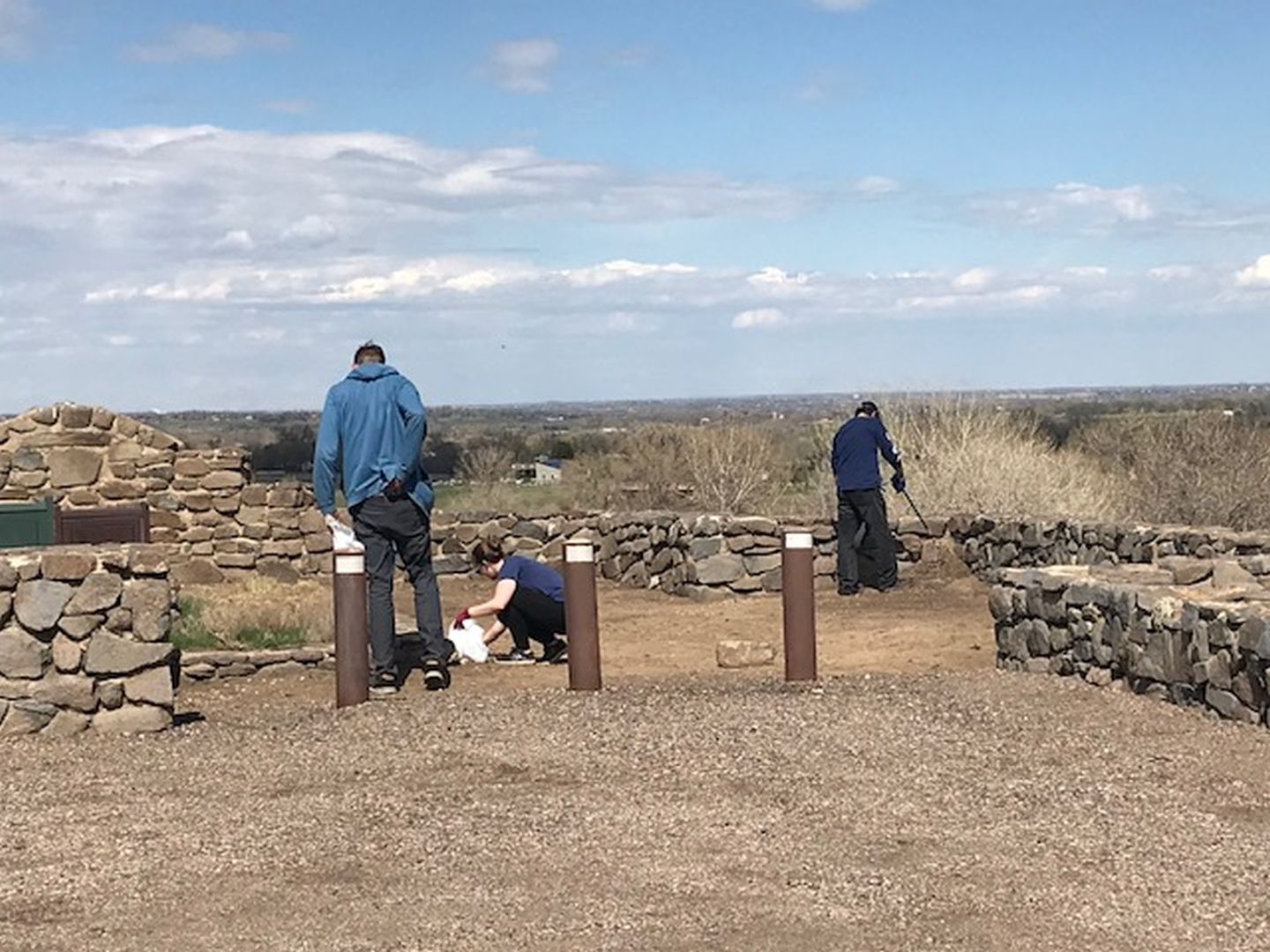 Three people picking up trash at a trailhead