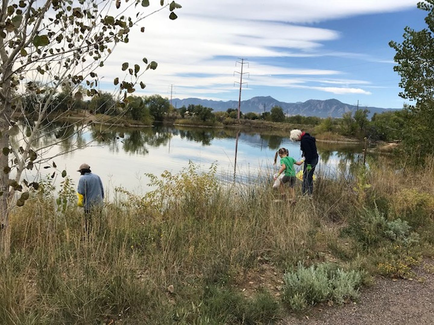 Three people looking for trash along the shoreline of a pond