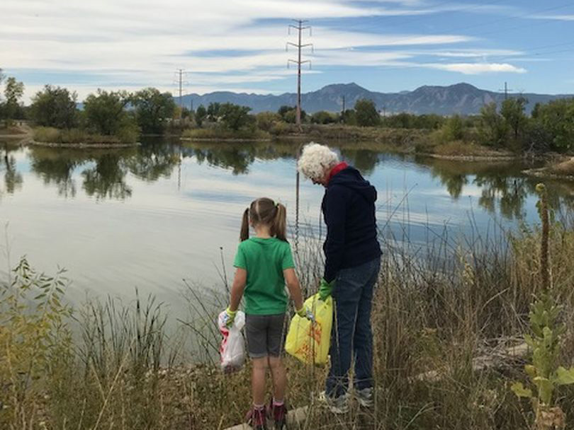 A young girl and an elderly woman looking for trash along a shoreline of a pond